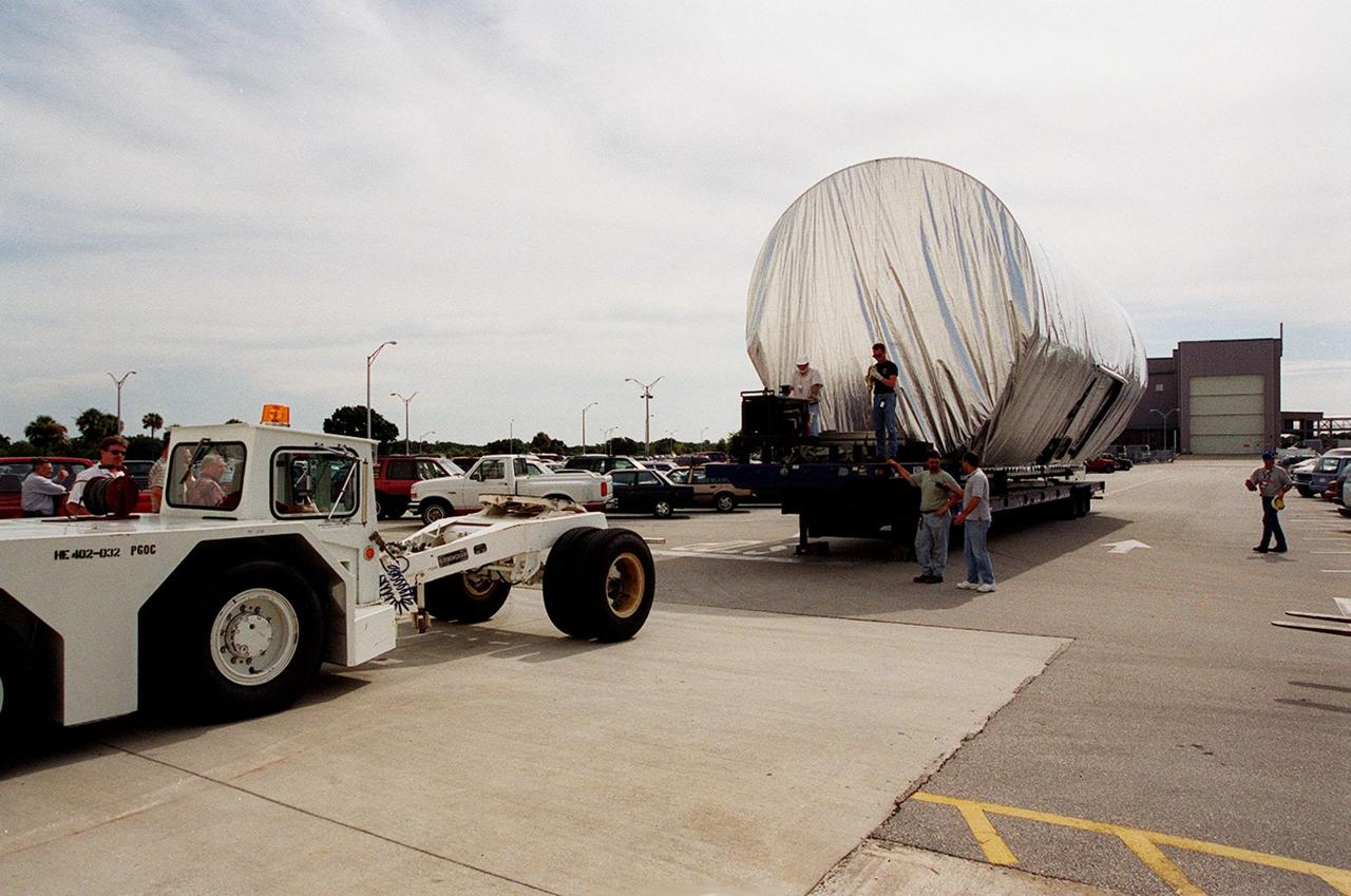 The P-1 truss, a component of the International Space Station, arrives in the parking lot outside the Operations and Checkout Building where it will undergo processing. The P-1 truss, scheduled to fly in spring of 2002, is part of a total 10-truss, girder-like structure on the Space Station that will ultimately extend the length of a football field. Astronauts will attach the 14-by-15 foot structure to the port side of the center truss, S0, during the spring assembly flight. The 33,000-pound P-1 will house the thermal radiator rotating joint (TRRJ) that will rotate the Station’s radiators away from the sun to increase their maximum cooling efficiency