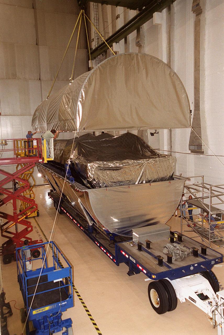 Inside the Operations and Checkout Building, an overhead crane lifts the top of the canister containing the P-1 truss, a component of the International Space Station. The truss, scheduled to fly in spring of 2002, is part of a total 10-truss, girder-like structure on the Station that will ultimately extend the length of a football field. Astronauts will attach the 14-by-15 foot structure to the port side of the center truss, S0, during the spring assembly flight. The 33,000-pound P-1 will house the thermal radiator rotating joint (TRRJ) that will rotate the Station’s radiators away from the sun to increase their maximum cooling efficiency