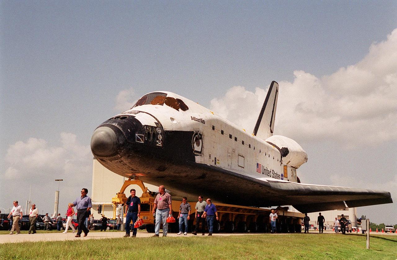 KENNEDY SPACE CENTER, FLA. -- KSC employees accompany the orbiter Atlantis as it is moved aboard an orbiter transporter to the Vehicle Assembly Building (VAB). In the background are OPF bays 1 and 2. In the VAB it will be lifted to vertical and placed aboard the mobile launcher platform (MLP) for stacking with the solid rocket boosters and external tank. Atlantis is scheduled to launch Sept. 8 on mission STS-106, the fourth construction flight to the International Space Station, with a crew of seven