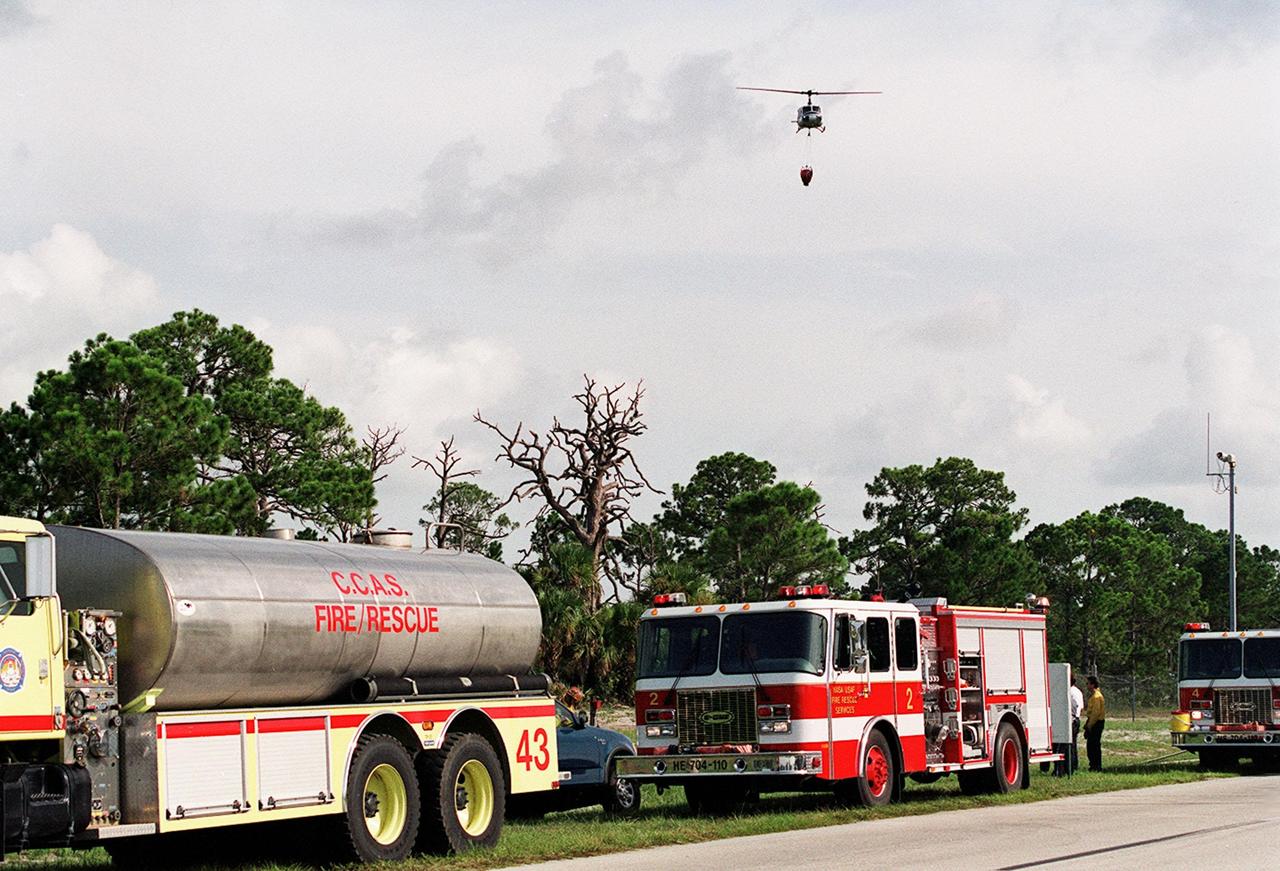 A NASA helicopter flies over fire-fighting equipment and personnel in order to drop its load of water on a wildfire at KSC. Before being extinguished, the fire burned about 20 acres at a site near gate 2C on Kennedy Parkway North (route 3)