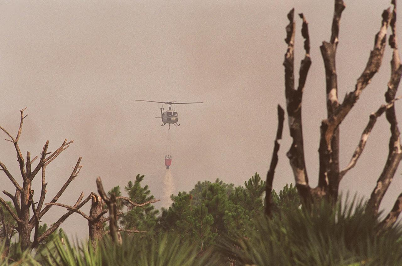 A NASA helicopter drops its cargo of water onto a wildfire at KSC. Before being extinguished, the fire burned about 20 acres at a site near gate 2C on Kennedy Parkway North (route 3)