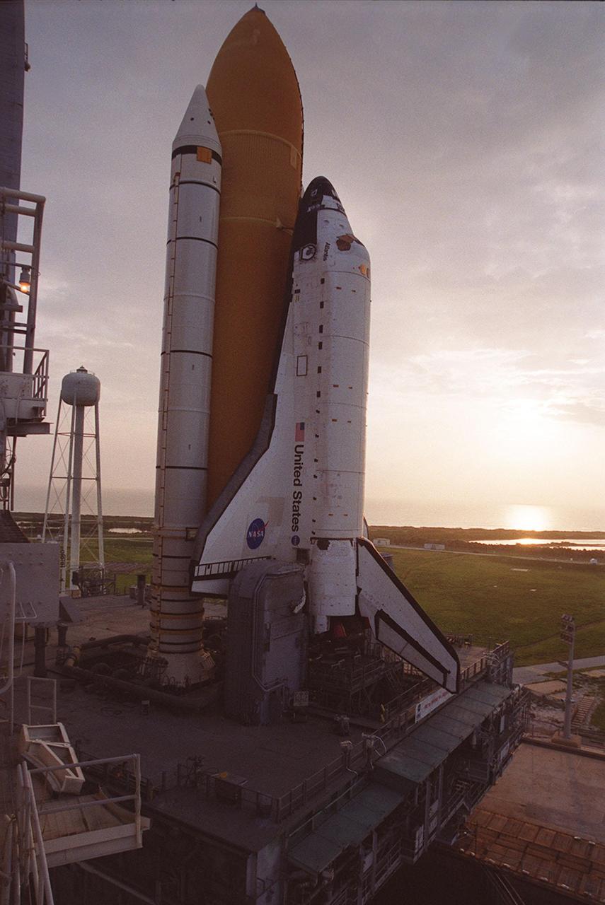 KENNEDY SPACE CENTER, Fla. -- The sun lights the early morning sky, revealing Space Shuttle Atlantis, atop the Mobile Launcher Platform and Crawler-Transporter, at Launch Pad 39B. It started its 8-hour rollout from the Vehicle Assembly Building high bay 2 (Safe Haven) at 11:20 p.m., Aug. 13, arriving shortly after 7 a.m. Aug. 14. At its immediate left is the 290-foot high water tank that holds 300,000 gallons of water, part of the sound suppression system at the pad. At the edge of the photo can be seen part of the Rotating Service Structure. Atlantis is scheduled for launch Sept. 8 at 8:31 a.m. EDT on mission STS-106.