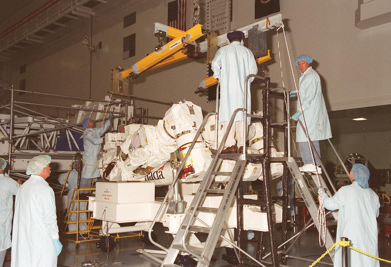 Workers in the Space Station Processing Facility help maneuver an overhead crane above the Canadian Space Agency’s Space Station Remote Manipulator System (SSRMS). The crane will lift and transfer the SSRMS to a test stand where it will be mated to its payload carrier. This pallet will later be installed into the payload bay of Space Shuttle Endeavour for launch to the International Space Station on STS-100 in April 2001. The 56-foot-long arm will be the primary means of transferring payloads between the orbiter payload bay and the Station. Its three segments comprise seven joints for highly flexible land precise movement, making it capable of moving around the Station’s exterior like an inchworm