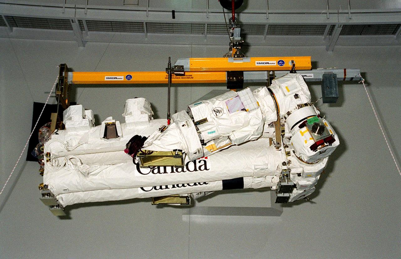  An overhead crane in the Space Station Processing Facility carries the Canadian Space Agency’s Space Station Remote Manipulator System (SSRMS) through the air to a test stand where it will be mated to its payload carrier. This pallet will later be installed into the payload bay of Space Shuttle Endeavour for launch to the International Space Station on STS-100 in April 2001. The 56-foot-long arm will be the primary means of transferring payloads between the orbiter payload bay and the Station. Its three segments comprise seven joints for highly flexible land precise movement, making it capable of moving around the Station’s exterior like an inchworm