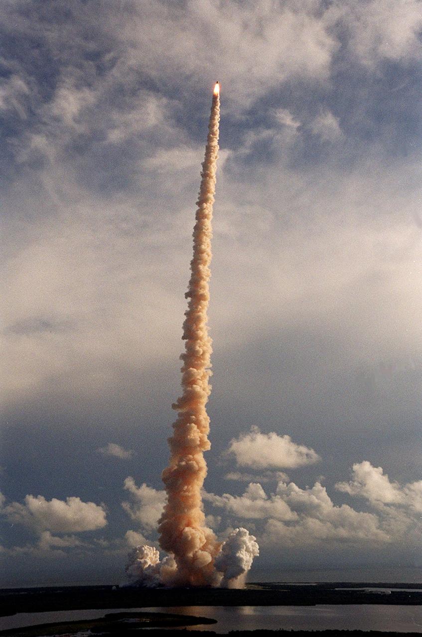 KENNEDY SPACE CENTER, Fla. -- Looking like a lighted taper against a cloud-streaked sky, Space Shuttle Atlantis belches a column of smoke as it blasts into space. In the foreground are patches of water and marsh between the Mosquito Lagoon on the north and Banana Creek on the south. In the background is the Atlantic Ocean. The perfect on-time liftoff of Atlantis occurred at 8:45:47 a.m. EDT. On the 11-day mission to the International Space Station, the seven-member crew will perform support tasks on orbit, transfer supplies and prepare the living quarters in the newly arrived Zvezda Service Module. The first long-duration crew, dubbed “Expedition One,” is due to arrive at the Station in late fall. Landing of Atlantis is targeted for 4:45 a.m. EDT on Sept. 19