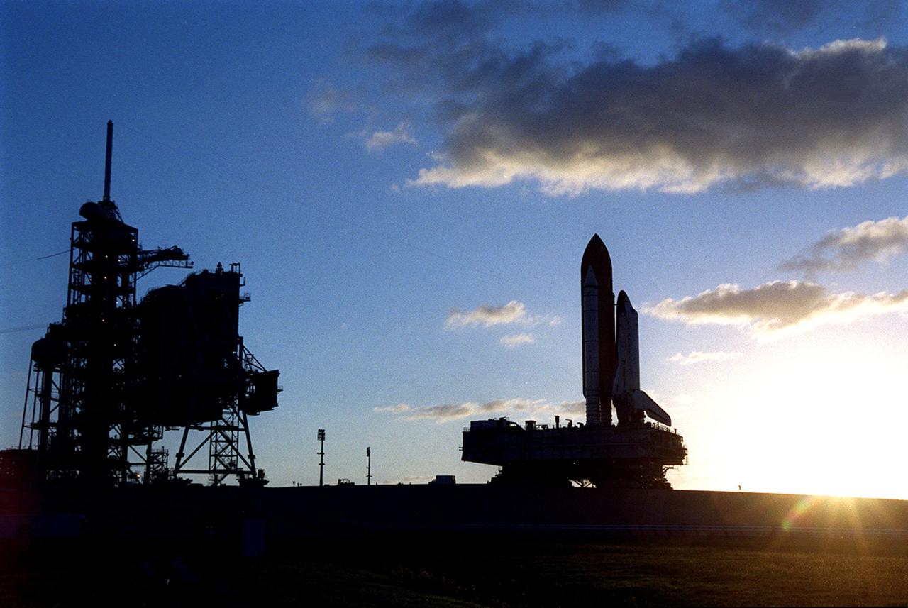 KENNEDY SPACE CENTER, Fla. -- As the sun crawls from below the horizon at right, Space Shuttle Discovery crawls up Launch Pad 39A and its resting spot next to the fixed service structure (FSS) (seen at left). The powerful silhouette dwarfs people and other vehicles near the FSS. Discovery is scheduled to launch Oct. 5 at 9:30 p.m. EDT on mission STS-92. Making the 100th Space Shuttle mission launched from Kennedy Space Center, Discovery will carry two pieces of hardware for the International Space Station, the Z1 truss, which is the cornerstone truss of the Station, and the third Pressurized Mating Adapter. Discovery also will be making its 28th flight into space, more than any of the other orbiters to date