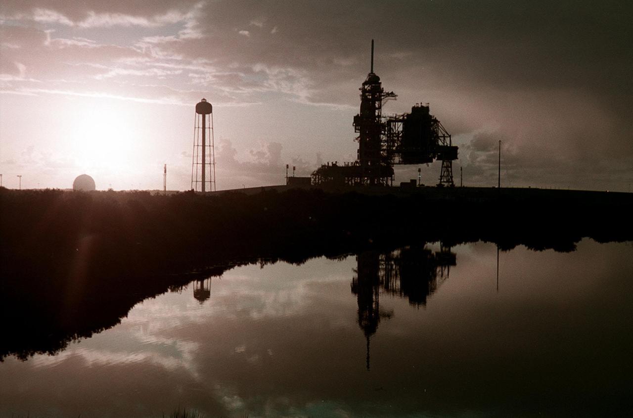 KENNEDY SPACE CENTER, Fla. --  Just after dawn, Launch Pad 39A is caught in silhouette and reflected in the water nearby. On the pad is Space Shuttle Discovery, waiting for launch on mission STS-92 Oct. 5, 2000. At the left of the pad is the 300,000-gallon water tank that is part of the sound suppression system during launches. At far left, the ball-shaped structure is a storage tank for one of the cryogenic liquid propellants of the orbiter’s main engines