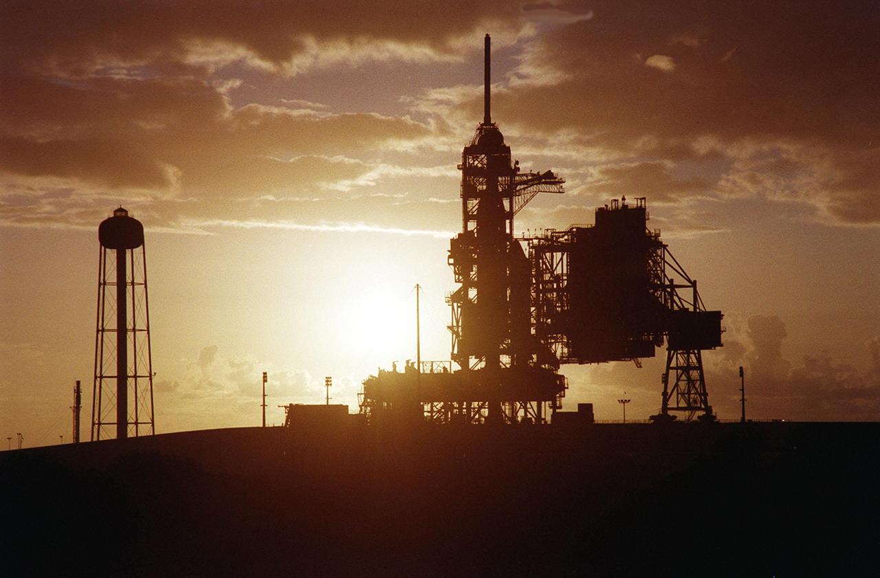 KENNEDY SPACE CENTER, Fla. -- While the morning sun paints the sky pale gold, the structures on Launch Pad 39A are silhouetted in brown. Space Shuttle Discovery can be seen on the other side of the Fixed Service Structure; the Rotating Service Structure at right is still open. At left is the 300,000-gallon water tank that is part of the sound suppression system during launches. Discovery will launch on mission STS-92 Oct. 5, 2000