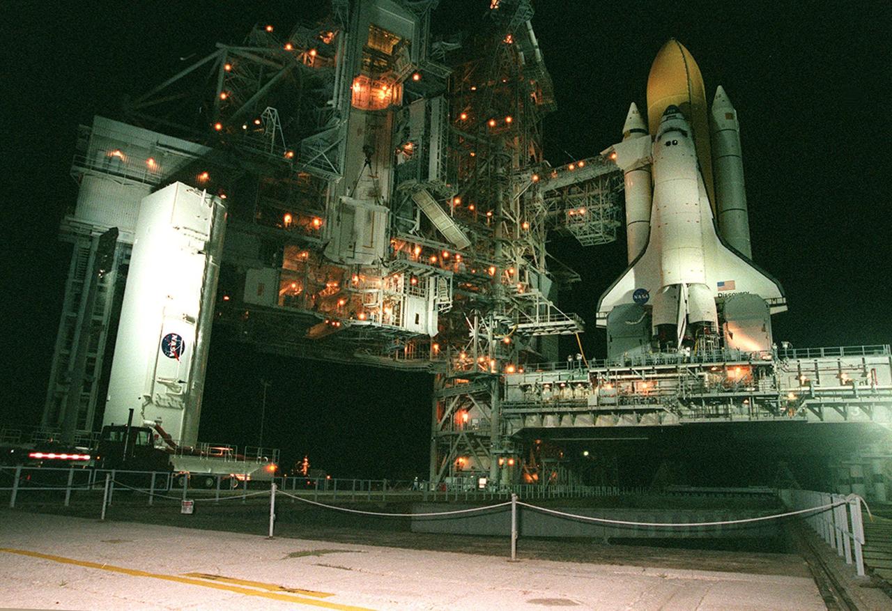 KENNEDY SPACE CENTER, Fla. --  At Launch Pad 39A, the payload canister at left draws closer to the Rotating Service Structure where it will be lifted to the Payload Changeout Room. There its cargo, the Integrated Truss Structure Z1, will be removed and later transferred to Space Shuttle Discovery’s payload bay. Discovery is at right, sitting atop the Mobile Launcher Platform. The Z1 truss is the first of 10 that will become the backbone of the International Space Station, eventually stretching the length of a football field. Along with its companion payload, the third Pressurized Mating Adapter, the Z1 is scheduled to be launched aboard Discovery Oct. 5 at 9:38 p.m. EDT