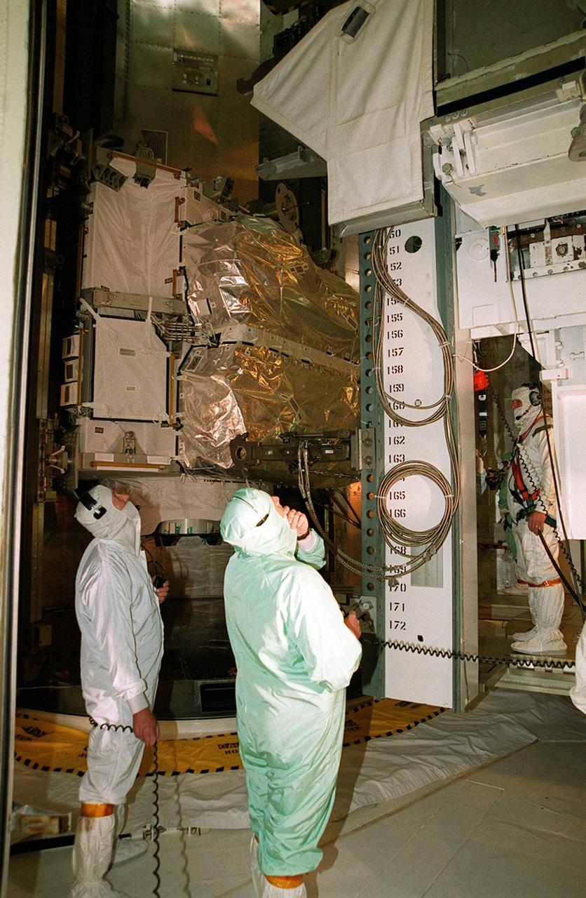 Inside the Payload Changeout Room (PCR), workers check the controls on movement of the Integrated Truss Structure Z1 behind them into the PCR from the payload canister. Once sealed inside the PCR, workers will get ready to move the Z1 into the payload bay of Space Shuttle Discovery. The Z1 truss is the first of 10 that will become the backbone of the International Space Station, eventually stretching the length of a football field. Along with its companion payload, the third Pressurized Mating Adapter, the Z1 is scheduled to be launched aboard Discovery Oct. 5 at 9:38 p.m. EDT