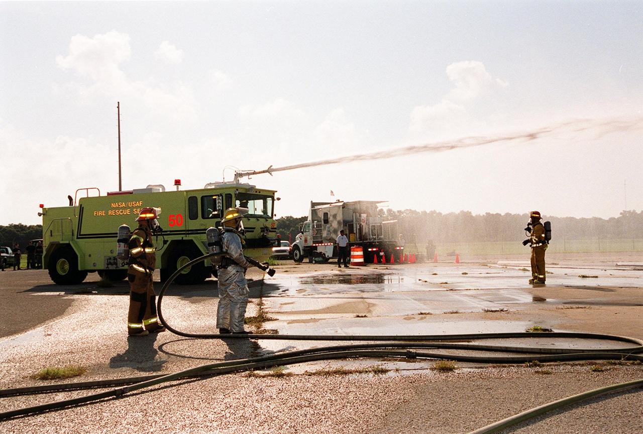 KENNEDY SPACE CENTER, FLA. -- During training exercises at Cape Canaveral Air Force Station Pad 30, firefighters with the Fire and Emergency Services at the Naval Station Mayport, Fla., wait while the NASA/USAF water carrier truck directs its water cannon toward a burning simulated aircraft (out of view).