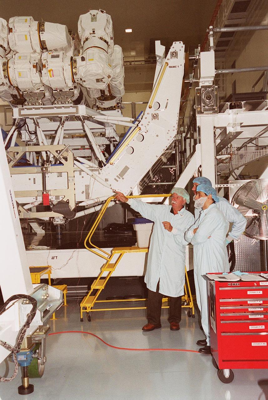 During Crew Equipment Interface Test for STS-100 crew members, a worker in the Space Station Processing Facility points to a nearby piece of hardware. Behind him is the Space Station Remote Manipulator System (SSRMS), also known as the Canadian arm. The SSRMS is the primary means of transferring payloads between the orbiter payload bay and the International Space Station for assembly. The 56-foot-long robotic arm includes two 12-foot booms joined by a hinge. Seven joints on the arm allow highly flexible and precise movement. Mission STS-100 is scheduled to launch April 19, 2001, carrying the SSRMS and Raffaello, a multi-purpose logistics module