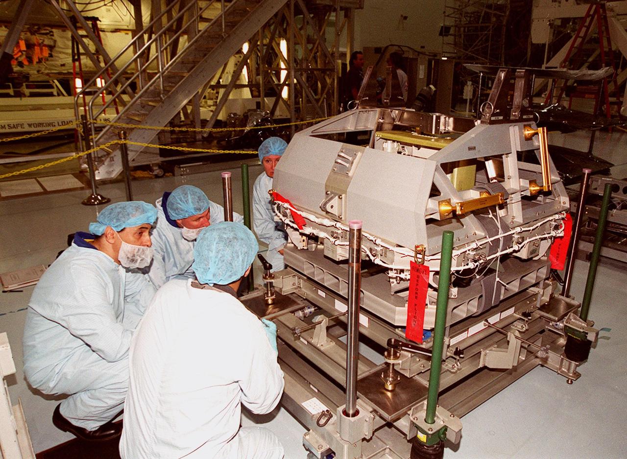 In the Space Station Processing Facility, STS-100 Mission Specialist Umberto Guidoni (left) and Commander Kent Rominger (center back), along with two workers, take a close look at equipment on the floor. Guidoni is with the European Space Agency. Mission STS-100, scheduled to launch April 19, 2001, will include the Multi-Purpose Logistics Module (MPLM) Raffaello and the Space Station Remote Manipulator System (SSRMS) as its payload. MPLMs are pressurized modules that will serve as the International Space Station's “moving vans,” carrying laboratory racks filled with equipment, experiments and supplies to and from the station aboard the Space Shuttle. The SSRMS is the primary means of transferring payloads between the orbiter payload bay and the International Space Station for assembly
