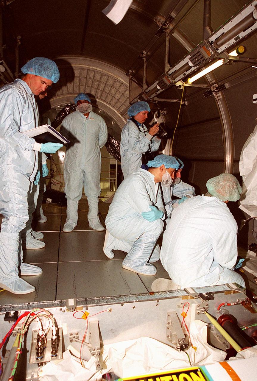 With workers looking on, STS-100 crew members check out equipment inside the Multi-Purpose Logistics Module Raffaello, located in the Space Station Processing Facility. Standing at center is Mission Specialist Umberto Guidoni, with the European Space Agency. Kneeling at right is Commander Kent Rominger. Mission STS-100, scheduled to launch April 19, 2001, will include Raffaello as well as the Space Station Remote Manipulator System (SSRMS) as its payload. MPLMs are pressurized modules that will serve as the International Space Station's “moving vans,” carrying laboratory racks filled with equipment, experiments and supplies to and from the station aboard the Space Shuttle. The SSRMS is the primary means of transferring payloads between the orbiter payload bay and the International Space Station for assembly