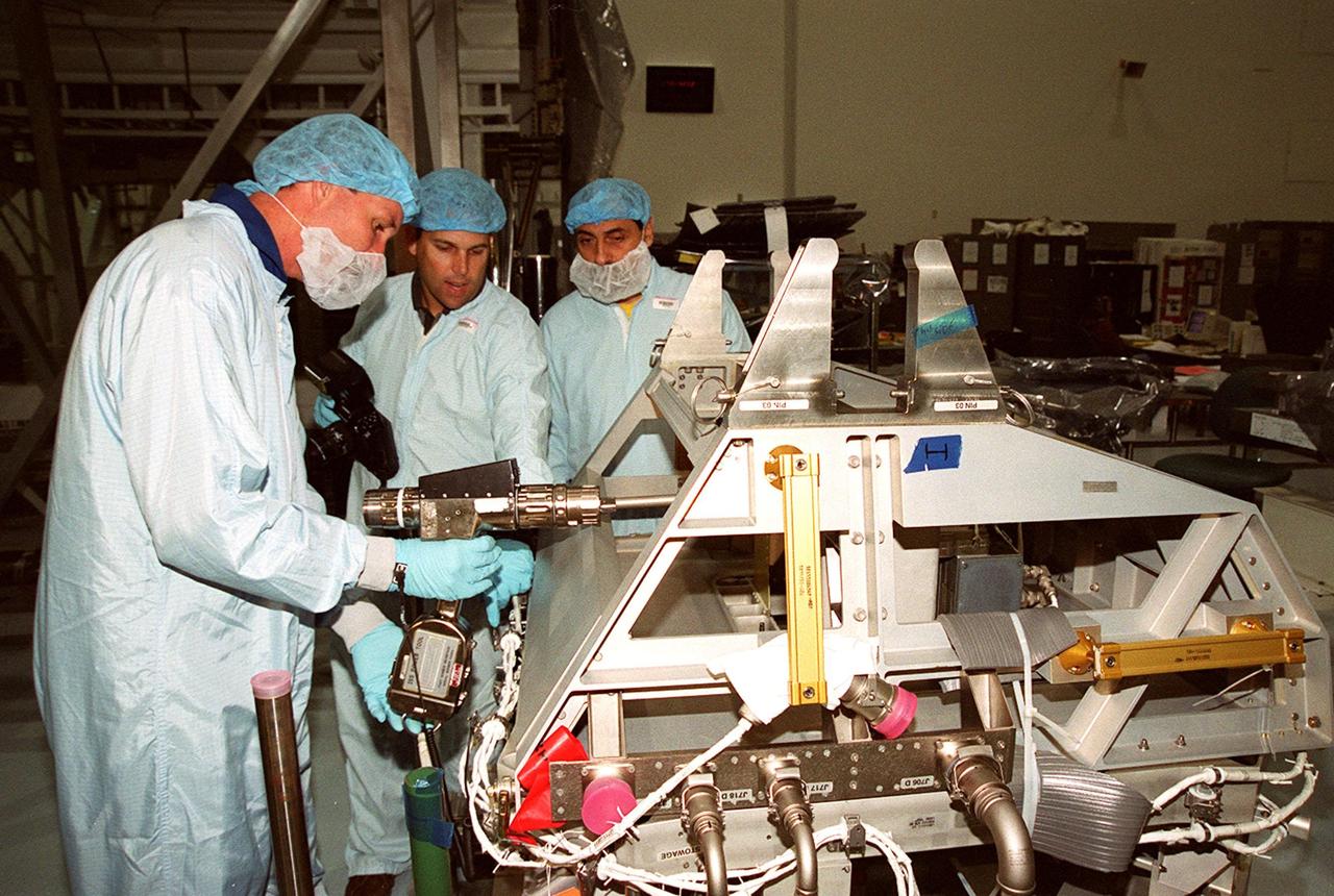 In the Space Station Processing Facility, STS-100 Commander Kent Rominger (left) tries out a piece of equipment while a worker (center) gives directions. Looking on at right is Mission Specialist Umberto Guidoni, with the European Space Agency. Mission STS-100, scheduled to launch April 19, 2001, will include Raffaello as well as the Space Station Remote Manipulator System (SSRMS) as its payload. MPLMs are pressurized modules that will serve as the International Space Station's “moving vans,” carrying laboratory racks filled with equipment, experiments and supplies to and from the station aboard the Space Shuttle. The SSRMS is the primary means of transferring payloads between the orbiter payload bay and the International Space Station for assembly