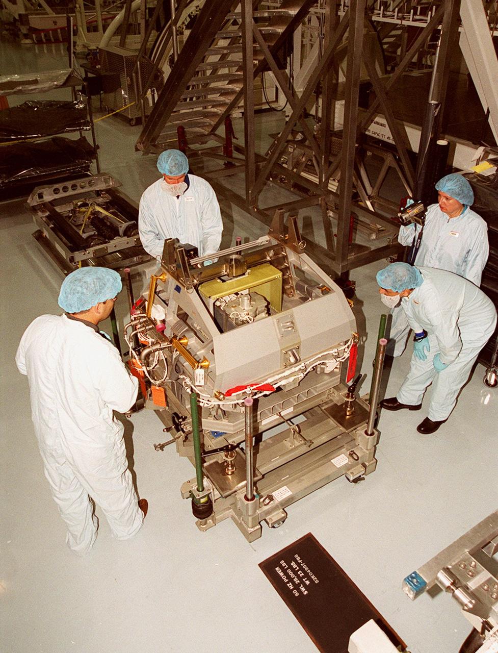 With workers (far left and far right) looking on, STS-100 Commander Kent Rominger tries out a piece of equipment while Mission Specialist Umberto Guidoni (leaning over) watches. Guidoni is with the European Space Agency. Mission STS-100, scheduled to launch April 19, 2001, will include Raffaello as well as the Space Station Remote Manipulator System (SSRMS) as its payload. MPLMs are pressurized modules that will serve as the International Space Station's “moving vans,” carrying laboratory racks filled with equipment, experiments and supplies to and from the station aboard the Space Shuttle. The SSRMS is the primary means of transferring payloads between the orbiter payload bay and the International Space Station for assembly
