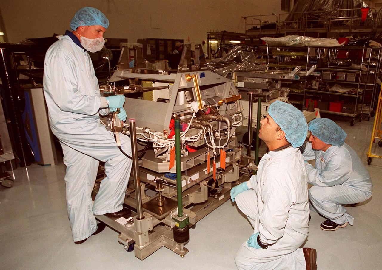 In the Space Station Processing Facility, STS-100 Commander Kent Rominger (left) listens to directions from the worker in the foreground. Another worker waits nearby. Mission STS-100, scheduled to launch April 19, 2001, will include Raffaello as well as the Space Station Remote Manipulator System (SSRMS) as its payload. MPLMs are pressurized modules that will serve as the International Space Station's “moving vans,” carrying laboratory racks filled with equipment, experiments and supplies to and from the station aboard the Space Shuttle. The SSRMS is the primary means of transferring payloads between the orbiter payload bay and the International Space Station for assembly