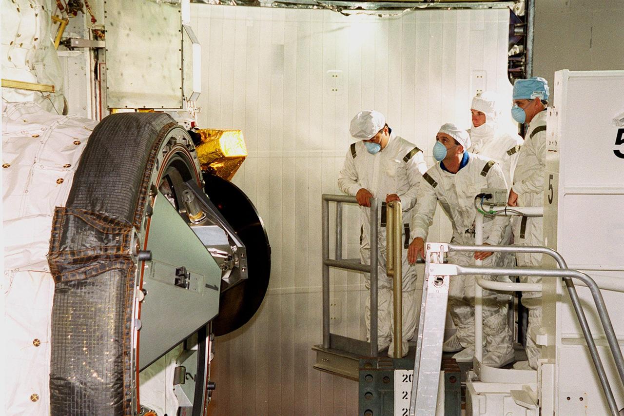 Members of the STS-92 crew look over the payload (left) in Space Shuttle Discovery’s payload bay. Left to right, in masks, are Mission Specialists Leroy Chiao, Peter J.K. “Jeff” Wisoff and William S. McArthur Jr. They and the other crew members Commander Brian Duffy, Pilot Pamela Ann Melroy and Mission Specialists Koichi Wakata of Japan, and Michael E. Lopez-Alegria are preparing for launch on Oct. 5, 2000. The mission is the fifth flight for the construction of the International Space Station. The payload includes the Integrated Truss Structure Z-1 and the third Pressurized Mating Adapter. During the 11-day mission, four extravehicular activities (EVAs), or space walks, are planned