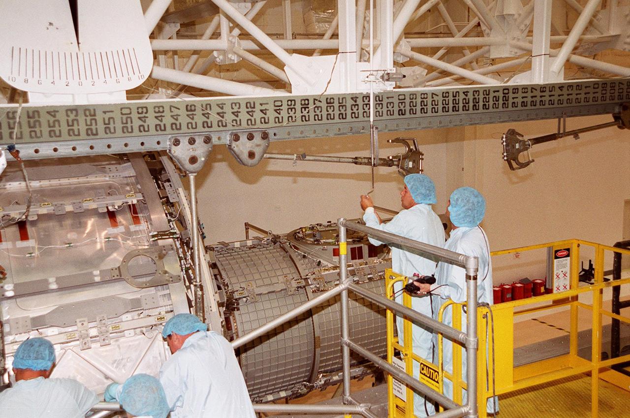 KENNEDY SPACE CENTER, FLA. -- A worker in the Operations and Checkout Building attaches the overhead crane to the Joint Airlock Module while another worker controls movement of the crane. The module will be lifted and placed in the payload canister for transfer to the Space Station Processing Facility. There the module will undergo more preflight processing for the STS-104 mission scheduled for launch aboard Space Shuttle Atlantis May 17, 2001. The Joint Airlock Module is the gateway from which crew members aboard the International Space Station will enter and exit the 470-ton orbiting research facility