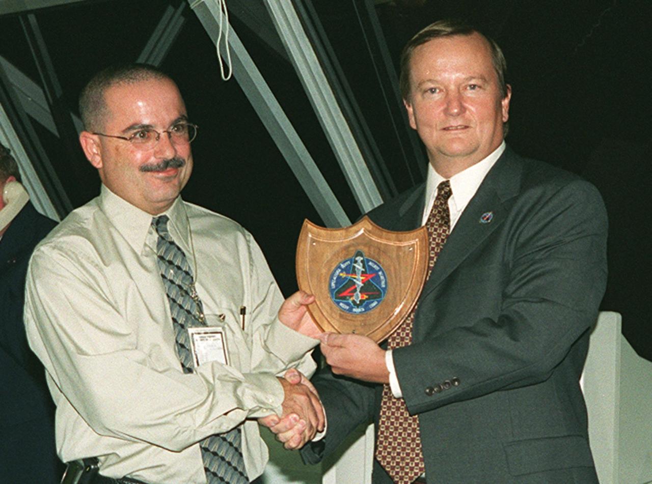 Jorge Rivera (center) receives a plaque and congratulations for his observatory powers from Shuttle Launch Director Mike Leinbach (right). A NASA external tank mechanical engineer, Rivera is the one who spotted the misplaced lock pin on Shuttle Discovery Oct. 10, shortly before the intended launch of mission STS-92, causing a scrub for safety reasons