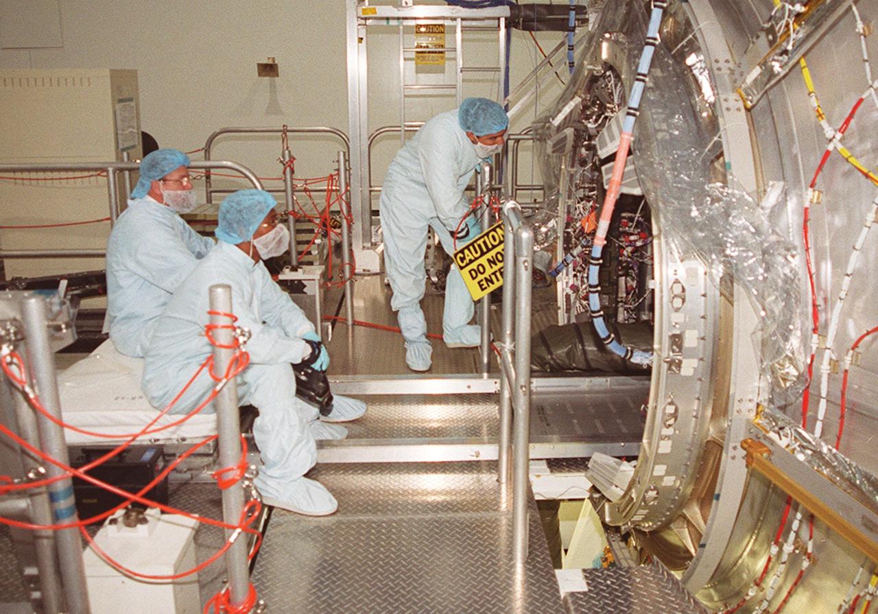 In the Space Station Processing Facility, workers at left watch while members of the STS-98 crew check out equipment inside the U.S. Lab, Destiny (at right). The crew comprises Commander Ken Cockrell, Pilot Mark Polansky and Mission Specialists Robert Curbeam, Thomas Jones and Marsha Ivins. They are taking part in Crew Equipment Interface Test activities, becoming familiar with equipment they will be handling during the mission. The mission will be transporting the Lab to the International Space Station with five system racks already installed inside of the module. With delivery of electronics in the lab, electrically powered attitude control for Control Moment Gyroscopes will be activated. The STS-98 launch is scheduled for Jan. 18, 2001