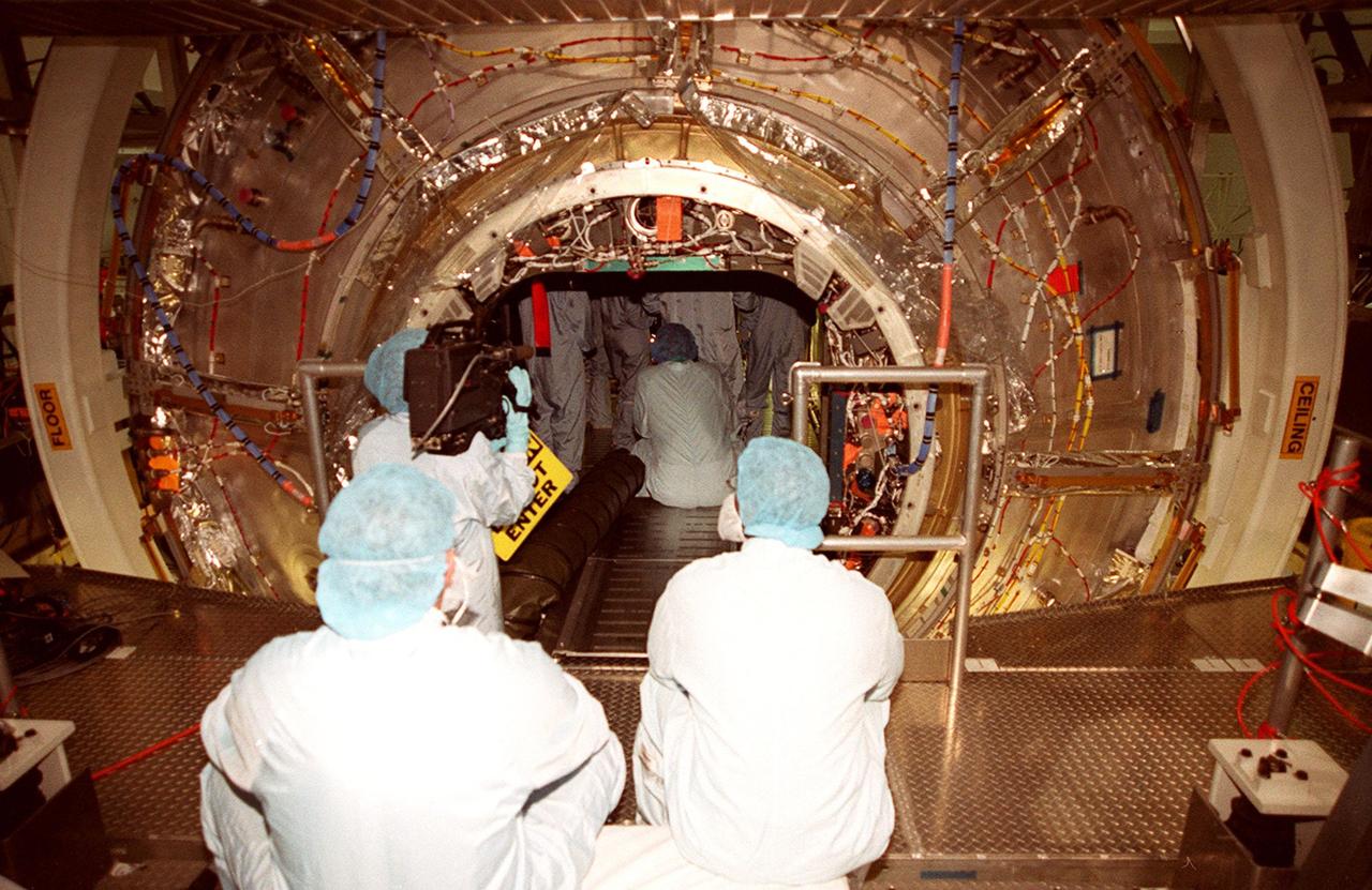 In the Space Station Processing Facility, workers in the foreground watch and wait while members of the STS-98 crew check out the U.S. Lab, Destiny in the background. The crew comprises Commander Ken Cockrell, Pilot Mark Polansky and Mission Specialists Robert Curbeam, Thomas Jones and Marsha Ivins. They are taking part in Crew Equipment Interface Test activities, becoming familiar with equipment they will be handling during the mission. The mission will be transporting the Lab to the International Space Station with five system racks already installed inside of the module. With delivery of electronics in the lab, electrically powered attitude control for Control Moment Gyroscopes will be activated. The STS-98 launch is scheduled for Jan. 18, 2001