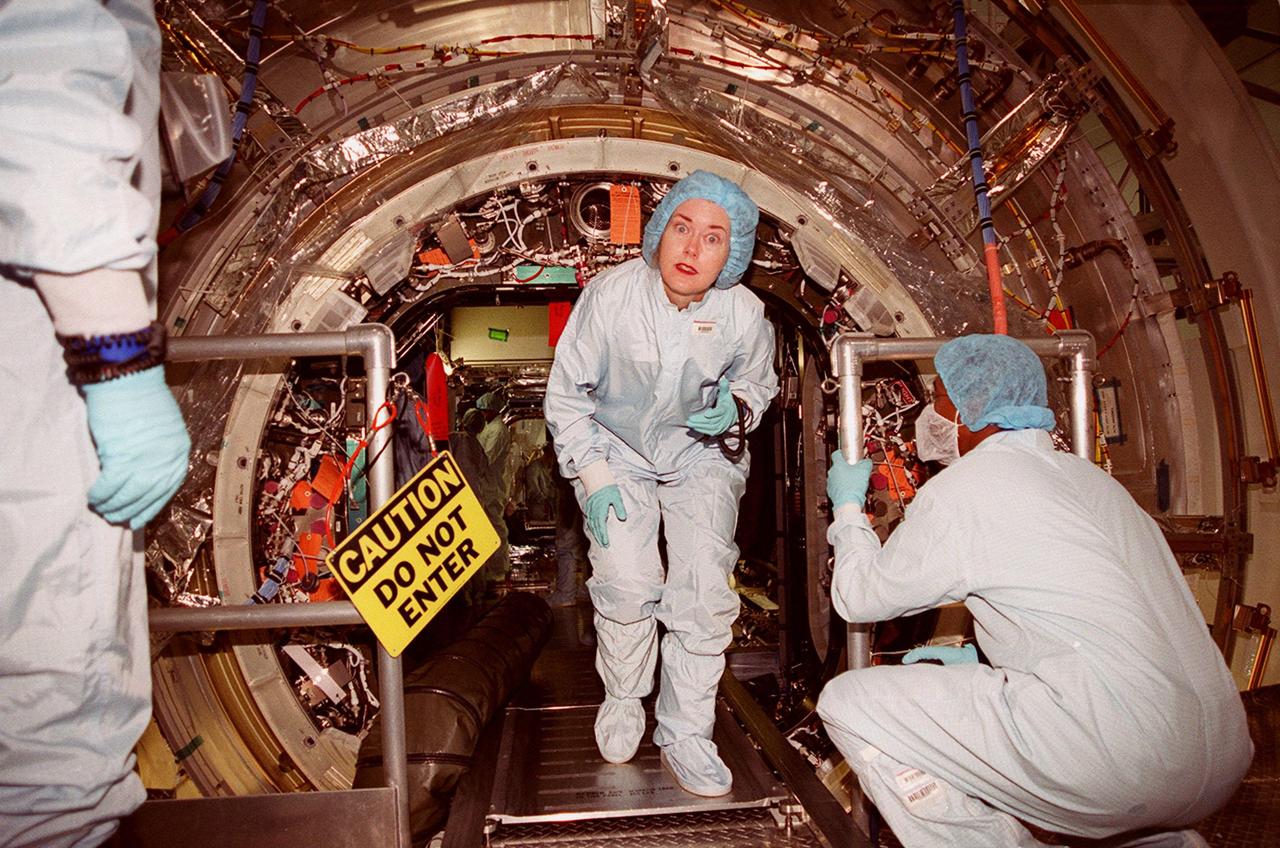In the Space Station Processing Facility, a worker is surprised by the camera as she exits the U.S. Lab, Destiny. Inside the lab is the STS-98 crew, which is taking part in Crew Equipment Interface Test activities, becoming familiar with equipment it will be handling during the mission. The crew comprises Commander Ken Cockrell, Pilot Mark Polansky and Mission Specialists Robert Curbeam, Thomas Jones and Marsha Ivins. The mission will be transporting the Lab to the International Space Station with five system racks already installed inside of the module. With delivery of electronics in the lab, electrically powered attitude control for Control Moment Gyroscopes will be activated. The STS-98 launch is scheduled for Jan. 18, 2001