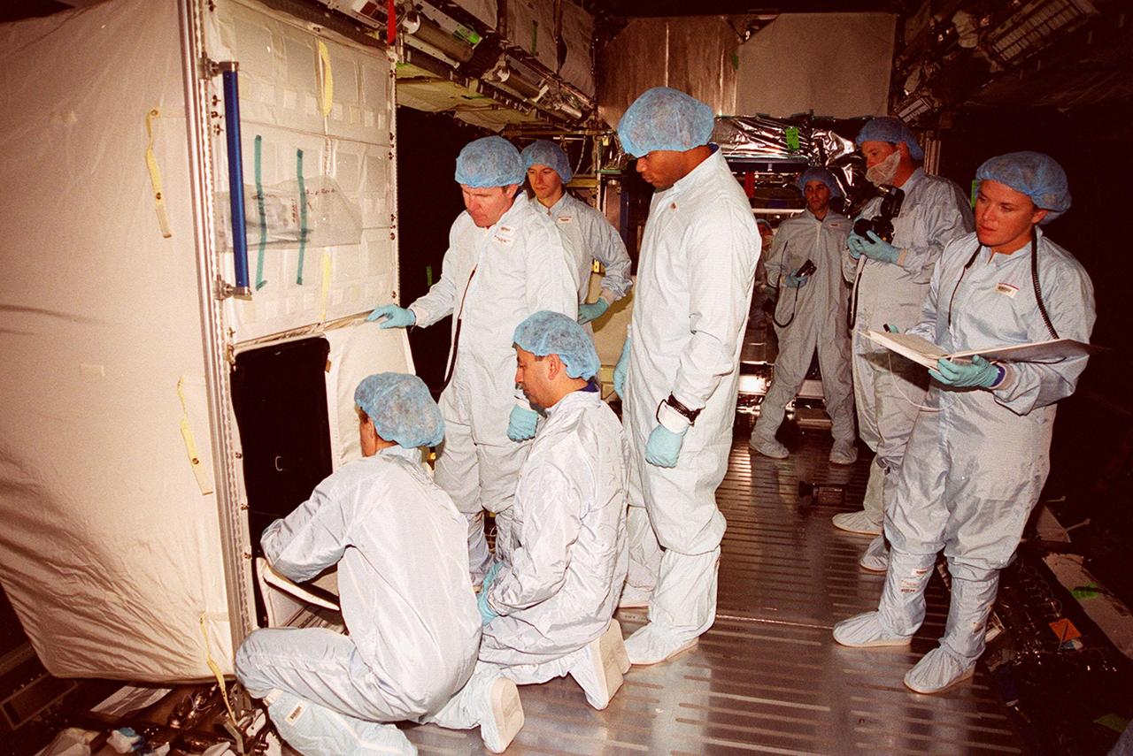 Inside the U.S. Lab, Destiny, members of the STS-98 crew work with technicians (in the background) to learn more about the equipment in the module. They are taking part in Crew Equipment Interface Test activities. At left, back to camera, is Mission Specialist Marsha Ivins. Standing are Mission Specialists Thomas Jones (left) and Robert Curbeam (right). Other crew members not seen are Commander Ken Cockrell and Pilot Mark Polansky. The mission will be transporting the Lab to the International Space Station with five system racks already installed inside of the module. With delivery of electronics in the lab, electrically powered attitude control for Control Moment Gyroscopes will be activated. The STS-98 launch is scheduled for Jan. 18, 2001