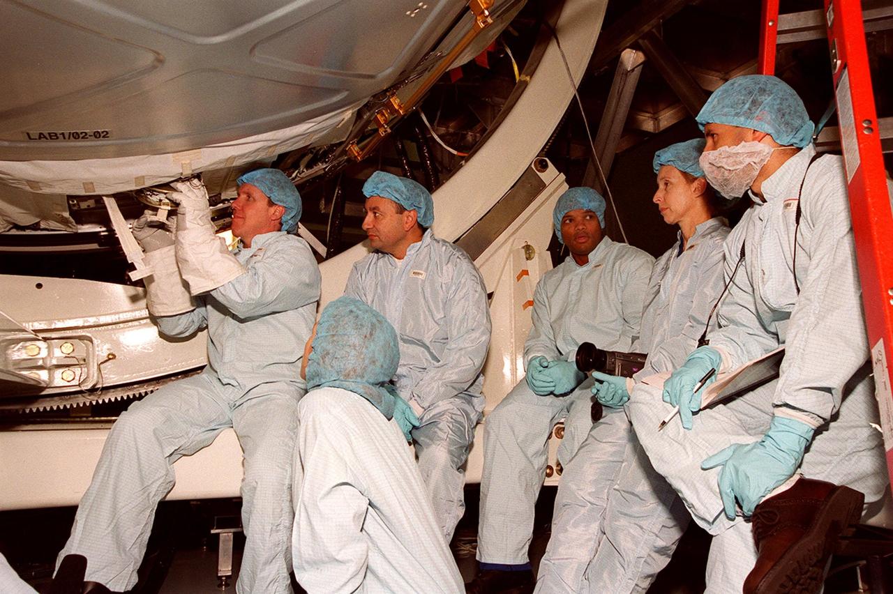 While trainers (bottom and right) look on, STS-98 Mission Specialist Thomas Jones practices handling a piece of equipment on the U.S. Lab, Destiny, while wearing the gloves he will wear in space. Watching next to him are other crew members Pilot Mark Polansky and Mission Specialists Robert Curbeam and Marsha Ivins. They are taking part in Crew Equipment Interface Test activities to become familiar with equipment they will be handling during the mission. With launch scheduled for Jan. 18, 2001, the STS-98 mission will be transporting the Lab to the International Space Station with five system racks already installed inside of the module. After delivery of electronics in the lab, electrically powered attitude control for Control Moment Gyroscopes will be activated