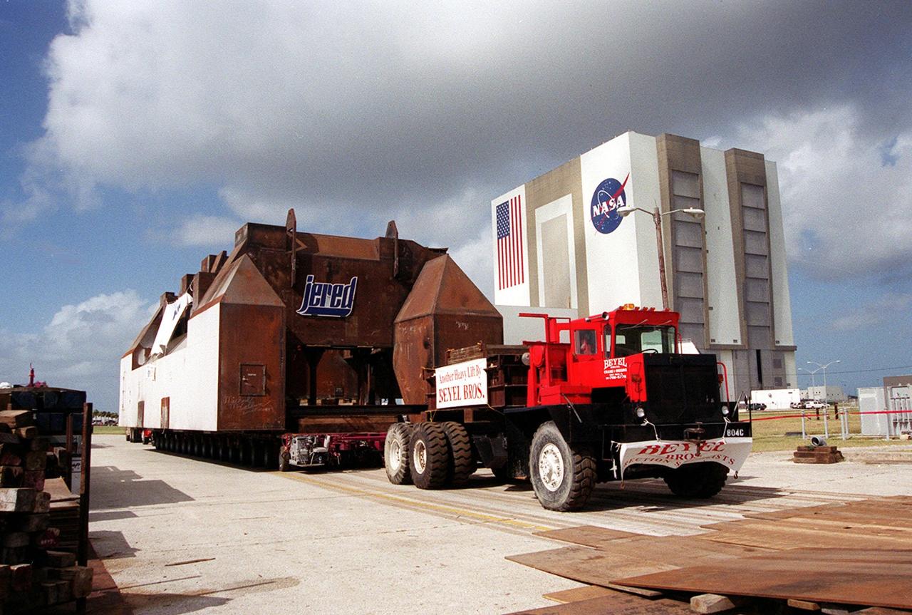 A launch table fabricated by Jered Industries in Georgia is ready for transfer to Launch Complex 37B, Cape Canaveral Air Force Station, after being moved off the barge that brought it to the turn basin in KSC’s Launch Complex 39 Area. In the background is the Vehicle Assembly Building. The table was built in support of the Delta Evolved Expendable Launch Vehicle (EELV) program, known as Delta IV. It was floated on the barge down the Intercoastal Waterway, through the Barge Canal to the turn basin. The table is approximately 70 feet long, 40 feet wide and 50 feet high, and weighs about 600,000 pounds. Accompanying the launch table on the barge are flame deflectors, which are also to be erected on pad 37B