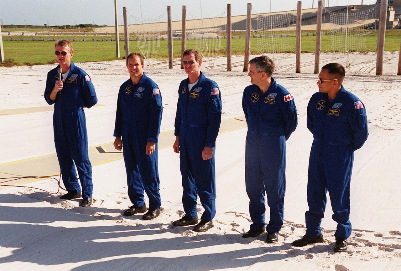 KENNEDY SPACE CENTER, Fla. -- Standing in the slidewire landing zone at Launch Pad 39B, the STS-97 crew respond to questions from the media. Commander Brent Jett (on left, with microphone) introduces the rest of the crew (left to right) Pilot Mike Bloomfield and Mission Specialists Joe Tanner, Marc Garneau and Carlos Noriega. Garneau is with the Canadian Space Agency. The nets suspended behind them are a braking system catch net for the slidewire baskets that provide emergency exit from the orbiter and Fixed Service Structure. The crew is at KSC to take part in Terminal Countdown Demonstration Test activities that include emergency egress training, familiarization with the payload, and a simulated launch countdown. Mission STS-97is the sixth construction flight to the International Space Station. Its payload includes the P6 Integrated Truss Structure and a photovoltaic (PV) module, with giant solar arrays that will provide power to the Station. The mission includes two spacewalks to complete the solar array connections. STS-97 is scheduled to launch Nov. 30 at about 10:05 p.m. EST