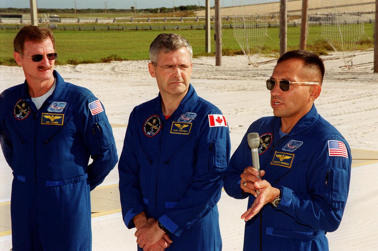 KENNEDY SPACE CENTER, Fla. -- From the slidewire landing zone at Launch Pad 39B, STS-97 Mission Specialist Carlos Noriega (at right, with microphone) describes the mission for the media. Next to him are Mission Specialists Joe Tanner (left) and Marc Garneau (center). The crew is at KSC to take part in Terminal Countdown Demonstration Test activities that include emergency egress training, familiarization with the payload, and a simulated launch countdown. The other crew members are Commander Brent Jett and Pilot Mike Bloomfield. Mission STS-97is the sixth construction flight to the International Space Station. Its payload includes the P6 Integrated Truss Structure and a photovoltaic (PV) module, with giant solar arrays that will provide power to the Station. The mission includes two spacewalks to complete the solar array connections. STS-97 is scheduled to launch Nov. 30 at about 10:05 p.m. EST
