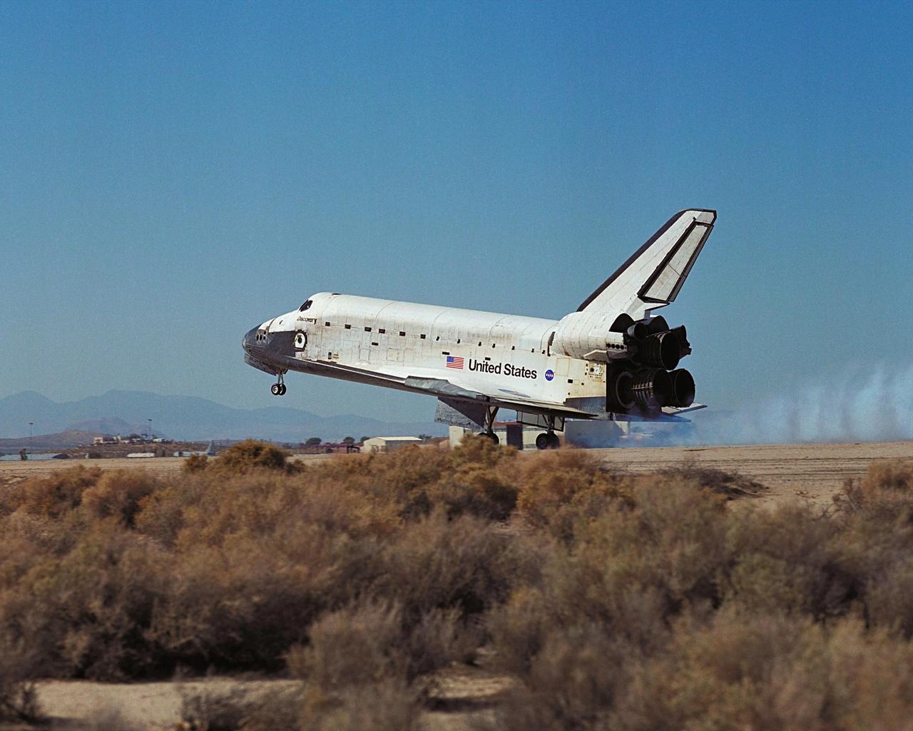 Viewed from the side, orbiter Discovery, with its seven-member crew, touches down on the landing strip at Edwards Air Force Base, Calif., after an 11-day mission to the International Space Station. The orbiter’s main landing gear touched down on EAFB runway 22 at 5 p.m. With the aid of its drag chute, Discovery came to a complete stop at 5:01 p.m. At the conclusion of mission STS-92, Discovery and crew had traveled about 5.3 million statute miles. Following vehicle safing and preliminary offloading efforts, workers will begin preparations for Discovery’s transcontinental ferry flight back to KSC on the back of NASA’s modified Boeing 747