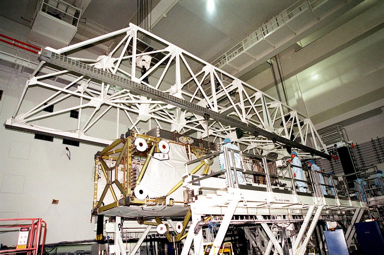 In the Space Station Processing Facility, workers attach an overhead crane to lift the P6 integrated truss segment from a workstand and move it to the payload transport canister for transfer to Launch Pad 39B. There it will be placed in Endeavour’s payload bay for launch on mission STS-97. The P6 comprises Solar Array Wing-3 and the Integrated Electronic Assembly, to be installed on the International Space Station. The Station’s electrical power system will use eight photovoltaic solar arrays, each 112 feet long by 39 feet wide, to convert sunlight to electricity. The solar arrays are mounted on a “blanket” that can be folded like an accordion for delivery. Once in orbit, astronauts will deploy the blankets to their full size. Gimbals will be used to rotate the arrays so that they will face the Sun to provide maximum power to the Space Station. Launch is scheduled for Nov. 30 at 10:06 p.m. EST