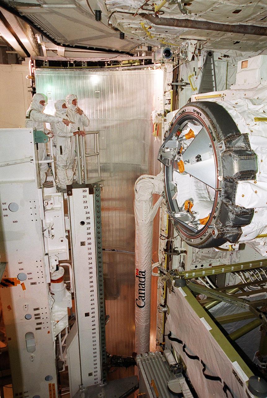 Members of the STS-97 crew look into Endeavour’s payload bay at some of the equipment that will be carried on the mission. On the left, pointing, is Mission Specialist Marc Garneau. Next to him (left to right) are Mission Specialist Carlos Noriega and Pilot Michael Bloomfield. At right center of the photo is the orbiter docking system (ODS). At left and below the ODS is the Canadian robotic arm that will be used during spacewalks on the mission to install solar arrays. Each more than 100 feet long, the arrays will capture energy from the sun and convert it to power for the Station. STS-97 is scheduled to launch Nov. 30 at about 10:06 p.m. EST