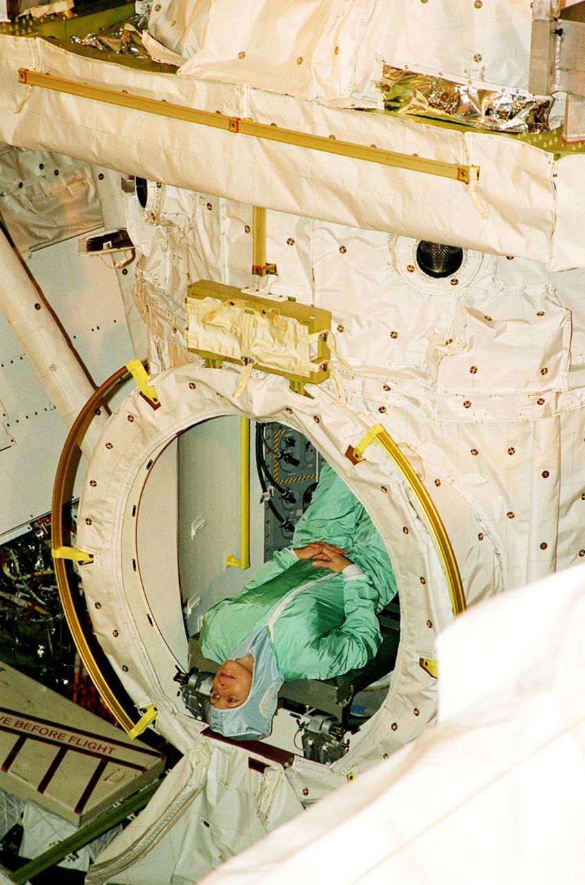 KENNEDY SPACE CENTER, FLA. -- STS-98 Mission Specialist Marsha Ivins takes a topsy-turvy look at the EVA hatch in the Orbiter Docking System, which is already installed in the payload bay of orbiter Atlantis. She and the rest of the crew are at KSC for Crew Equipment Interface Test activities. Launch on mission STS-98 is scheduled for Jan. 18, 2001. It will be transporting the U.S. Lab, Destiny, to the International Space Station with five system racks already installed inside of the module. After delivery of electronics in the lab, electrically powered attitude control for Control Moment Gyroscopes will be activated
