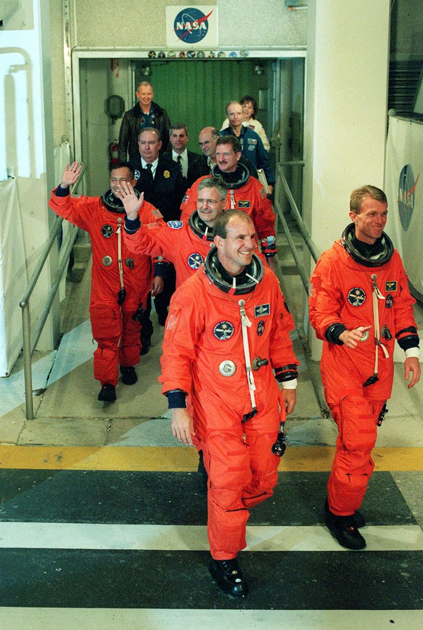 Eager to speed into space, the STS-97 crew hurries out of the Operations and Checkout Building for the ride to Launch Pad 39B. Leading the way are Pilot Michael Bloomfield (left) and Commander Brent Jett (right). In the middle is Mission Specialist Marc Garneau (waving), who is with the Canadian Space Agency. Behind are Mission Specialists Carlos Noriega (left, waving) and Joseph Tanner. Mission STS-97 is the sixth construction flight to the International Space Station. It is transporting the P6 Integrated Truss Structure that comprises Solar Array Wing-3 and the Integrated Electronic Assembly, to be installed on the Space Station. The solar arrays are mounted on a “blanket” that can be folded like an accordion for delivery. Once in orbit, astronauts will deploy the blankets to their full size. The 11-day mission includes two spacewalks to complete the solar array connections. The Station’s electrical power system will use eight photovoltaic solar arrays, each 112 feet long by 39 feet wide, to convert sunlight to electricity. Gimbals will be used to rotate the arrays so that they will face the Sun to provide maximum power to the Space Station. Launch is scheduled for Nov. 30 at 10:06 p.m. EST