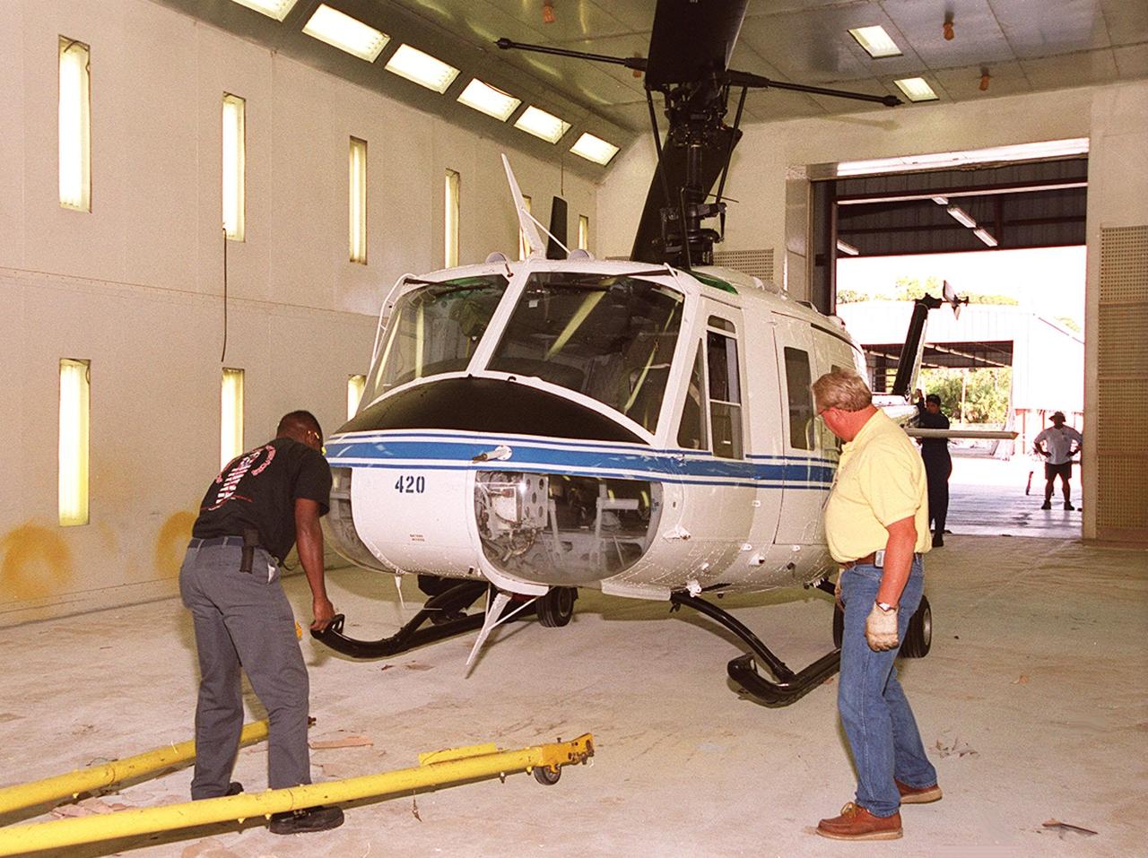 KENNEDY SPACE CENTER, FLA. -- Workers get ready to move a NASA UH-1H helicopter outside. They have been painting the blades of four NASA UH-1H helicopters, changing the black to a pattern of white and yellow stripes. The pattern provides better visibility in smoke and fire conditions. When the rotors are turning, the stripes create a yellow and white circle that is more easily seen by a second helicopter from above. The helicopters, primarily used for security and medical evacuation for NASA, will be used to deliver water via buckets during brush fires. The change was made to comply with U.S. Fish and Wildlife and Department of Forestry regulations for helicopter-assisted fire contro