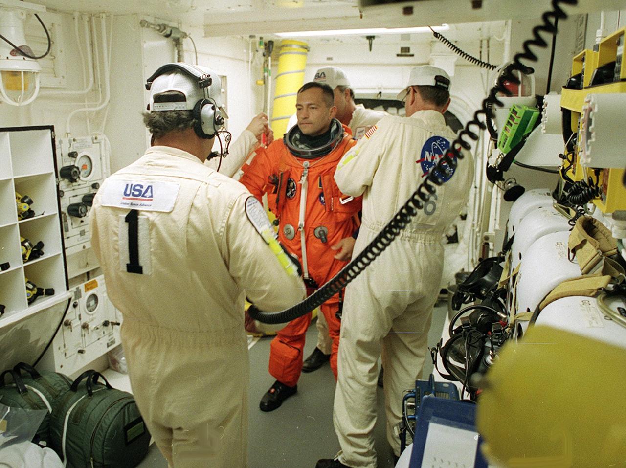 In the White Room, STS-97 Mission Specialist Carlos Noriega Tanner prepares for entry into Space Shuttle Endeavour with the help of the Closeout Crew, Travis Thompson (left) and Jack Burritt (right). Space Shuttle Endeavour is targeted to launch Nov. 30 at 10:06 p.m. EST for the six construction flight to the International Space Station. Endeavour is transporting the P6 Integrated Truss Structure that comprises Solar Array Wing-3 and the Integrated Electronic Assembly, to provide power to the Space Station. After the 11-day mission, which includes three spacewalks, it is expected to land at KSC Dec. 11 at 6:19 p.m. EST