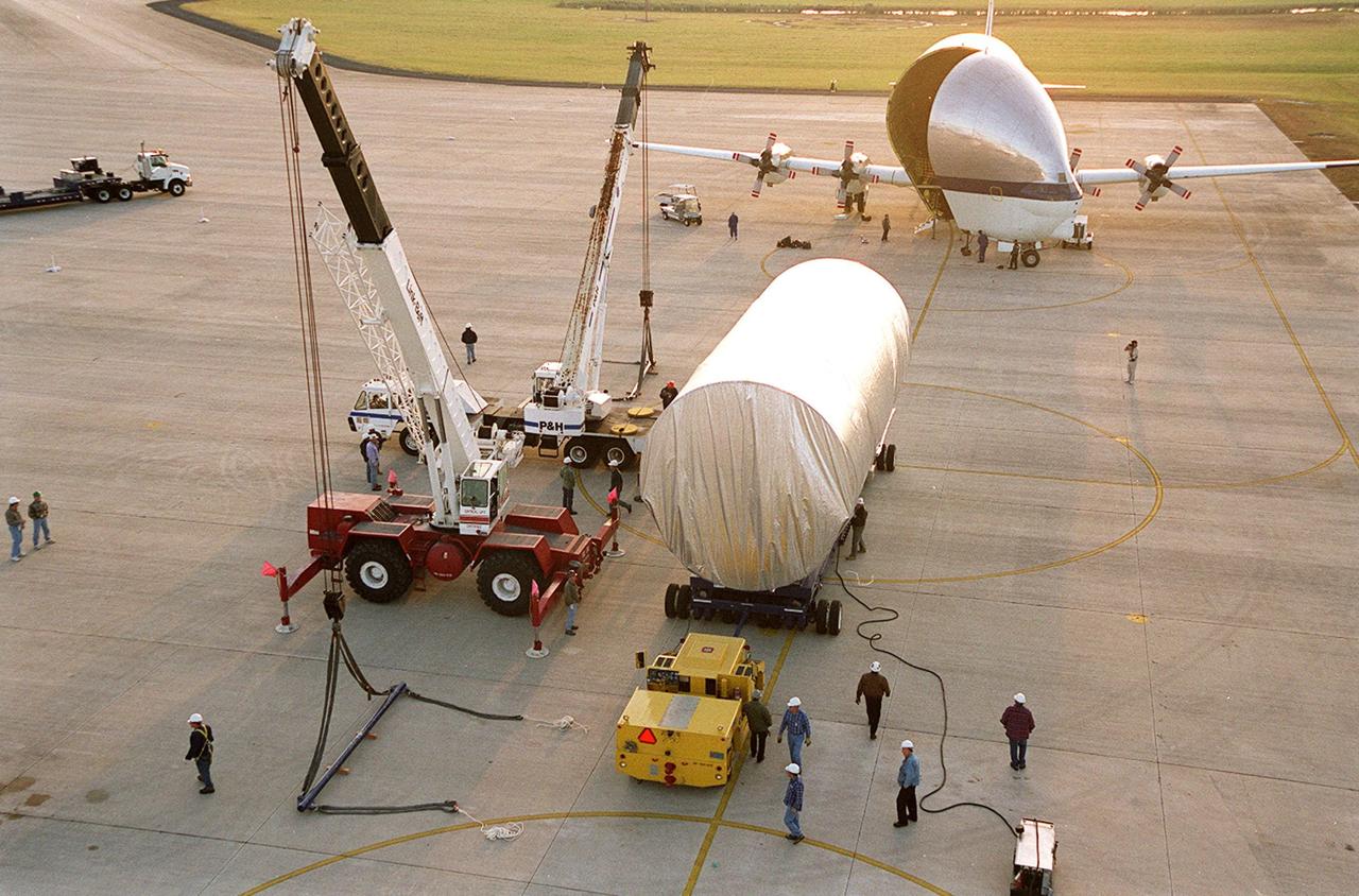 The Integrated Truss Structure S3 waits on the parking apron of the Shuttle Landing Facility after being offloaded from the Super Guppy aircraft in the background. The truss will be moved to a transporter and taken to the Operations and Checkout Building. The second starboard truss segment of the International Space Station, the S3 truss is scheduled to be added to the Station in April 2003