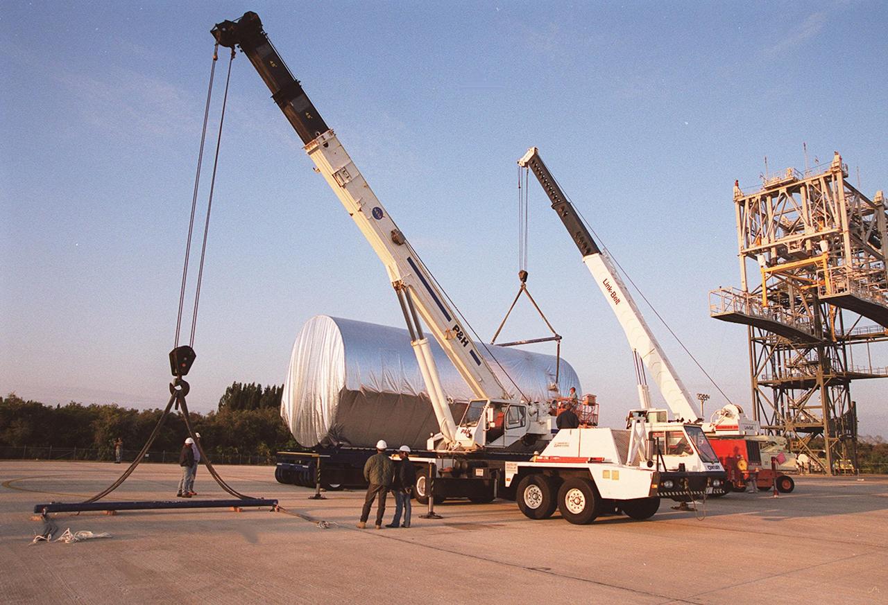 Cranes move toward the Integrated Truss Structure S3 as it sits on the parking apron of the Shuttle Landing Facility after being offloaded from the Super Guppy aircraft. The truss will be moved to a transporter and taken to the Operations and Checkout Building. The second starboard truss segment of the International Space Station, the S3 truss is scheduled to be added to the Station in April 2003