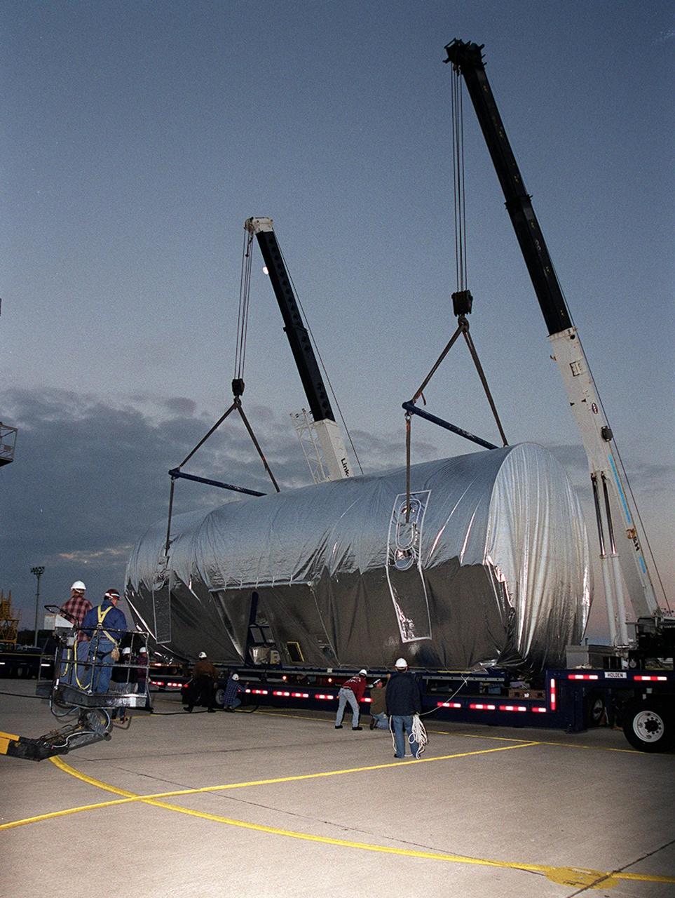 At the Shuttle Landing Facility, cranes position the Integrated Truss Structure S3 onto a flatbed trailer for transport to the Operations and Checkout Building. The S3 arrived aboard a Super Guppy aircraft. The second starboard truss segment of the International Space Station, the S3 truss is scheduled to be added to the Station in April 2003