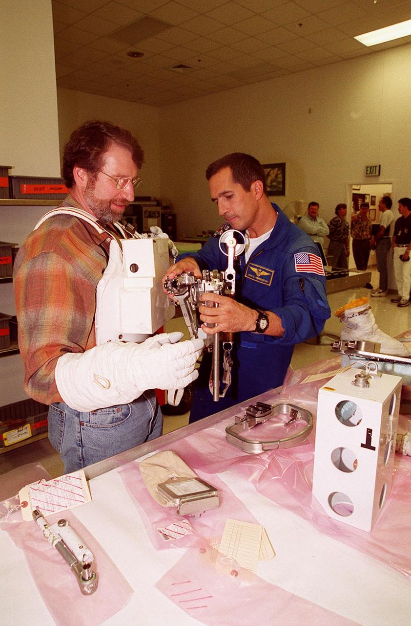 KENNEDY SPACE CENTER, FLA. --  Astronaut John Herrington (right) helps Norm Abram try on a tool carrier used in space. Abram is the master carpenter on television’s "This Old House."  He is at KSC to film an episode of the series