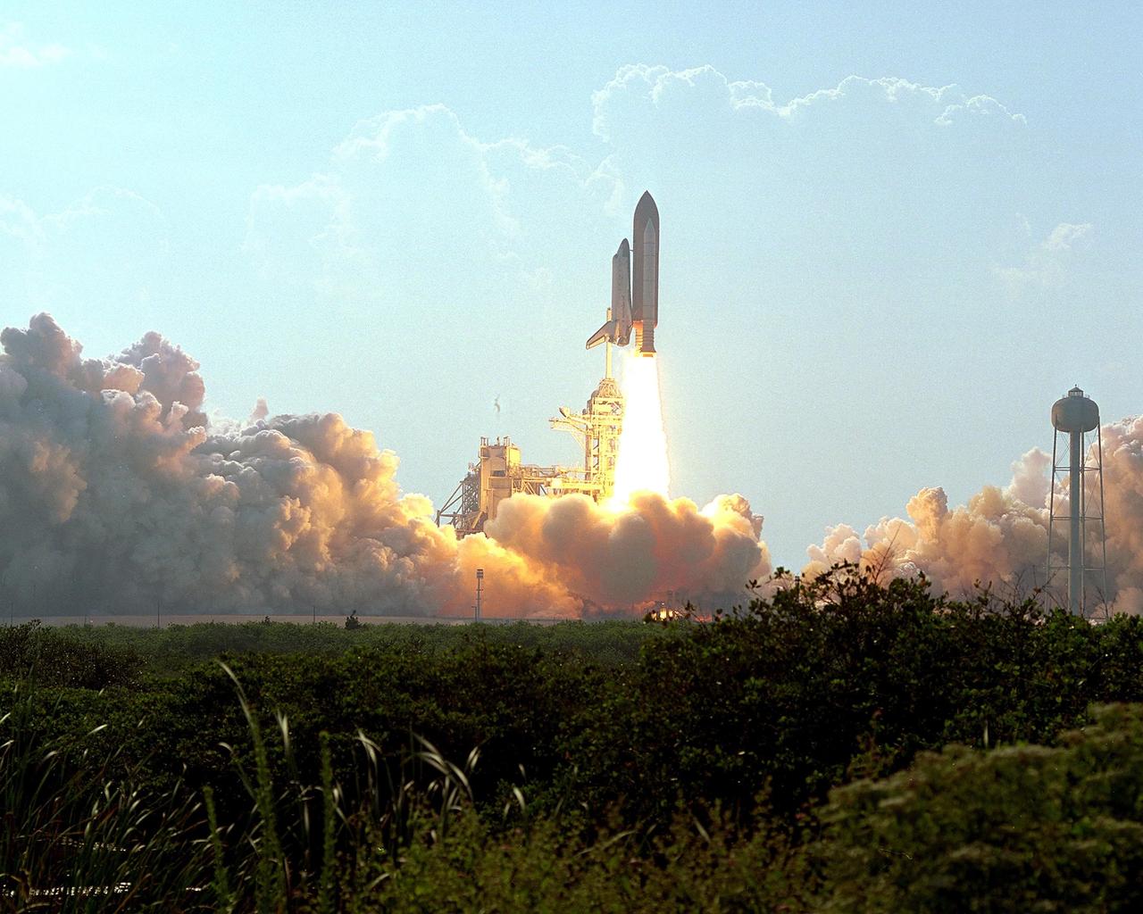 KENNEDY SPACE CENTER, Fla. -- Clouds of smoke and steam roll across the ground as Space Shuttle Discovery hurtles into the blue sky against a backdrop of cumulus clouds. Liftoff from Launch Pad 39A occurred at 5:10:14 p.m. EDT. Besides the Shuttle crew of four, Discovery carries the Expedition Three crew who will replace Expedition Two on the Space Station. The mission payload includes the third flight of the Italian-built Multi-Purpose Logistics Module Leonardo, delivering additional scientific racks, equipment and supplies for the Space Station, and the Early Ammonia Servicer (EAS) tank. The EAS, which will be attached to the Station during two spacewalks, contains spare ammonia for the Station’s cooling system. The three-member Expedition Two crew will be returning to Earth aboard Discovery after a five-month stay on the Station