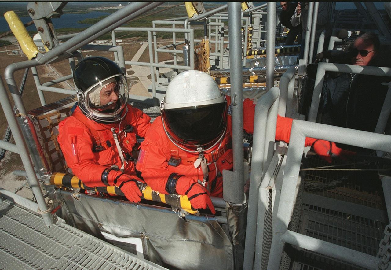 During emergency egress training at the 195-foot level of the Fixed Service Structure, Pilot Mark Polansky settles in the slidewire basket while Commander Ken Cockrell reaches for the release handle. The basket slides along a 1200-foot wire to the landing zone below and nearby bunker. The crew has been taking part in Terminal Countdown Demonstration Test activities, which include the simulated countdown and emergency egress training at the pad. STS-98 is the seventh construction flight to the International Space Station, carrying as payload the U.S. Lab Destiny, a key element in the construction of the ISS. Launch of STS-98 is scheduled for Jan. 19 at 2:11 a.m. EST
