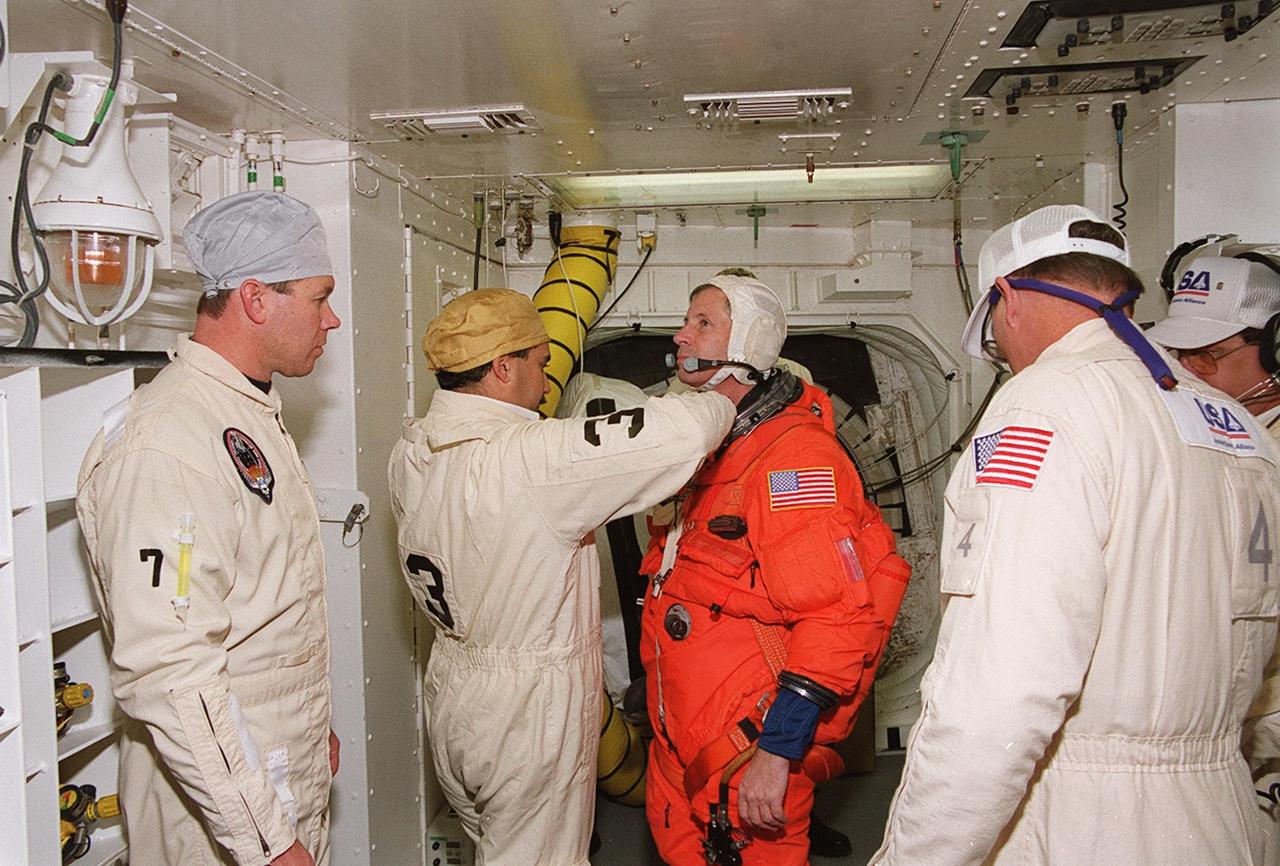In the White Room at Launch Pad 39A, STS-98 Commander Ken Cockrell (center) gets help from the closeout crew with his launch and entry suit before entering Atlantis for a simulated launch countdown. The White Room is an environmental chamber at the end of the orbiter access arm that mates with the orbiter to allow personnel to enter the orbiter’s crew compartment. The STS-98 crew is taking part in Terminal Countdown Demonstration Test activities, which also include emergency egress training at the pad. STS-98 is the seventh construction flight to the International Space Station, carrying as payload the U.S. Lab Destiny, a key element in the construction of the ISS. Launch of STS-98 is scheduled for Jan. 19 at 2:11 a.m. EST