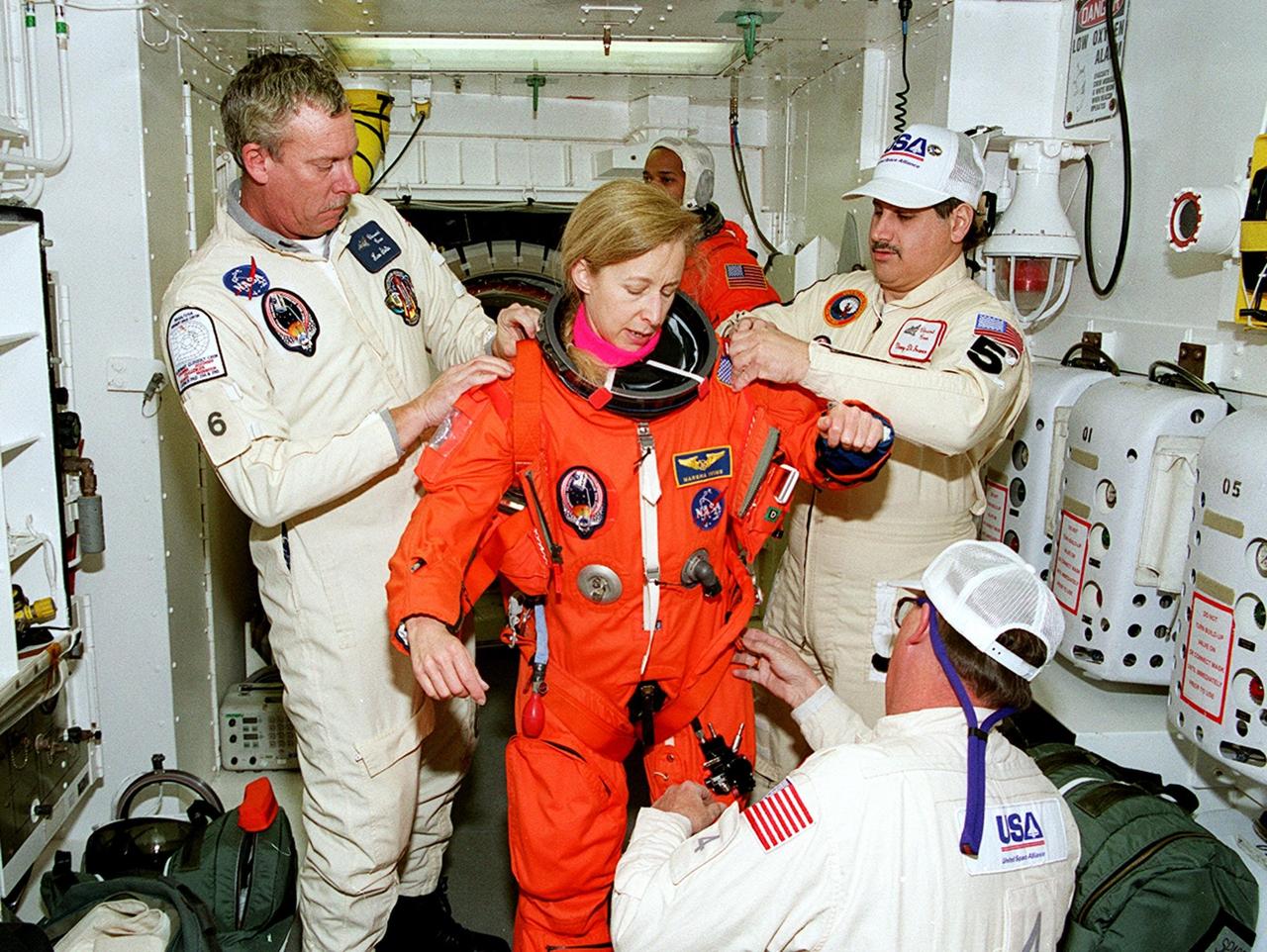 In the White Room, members of the closeout crew help STS-98 Mission Specialist Marsha Ivins (center) with her launch and entry suit before she enters Atlantis for a simulated launch countdown. The White Room is an environmental chamber at the end of the orbiter access arm that mates with the orbiter to allow personnel to enter the orbiter’s crew compartment. The STS-98 crew is taking part in Terminal Countdown Demonstration Test activities, which also include emergency egress training at the pad. STS-98 is the seventh construction flight to the International Space Station, carrying as payload the U.S. Lab Destiny, a key element in the construction of the ISS. Launch of STS-98 is scheduled for Jan. 19 at 2:11 a.m. EST