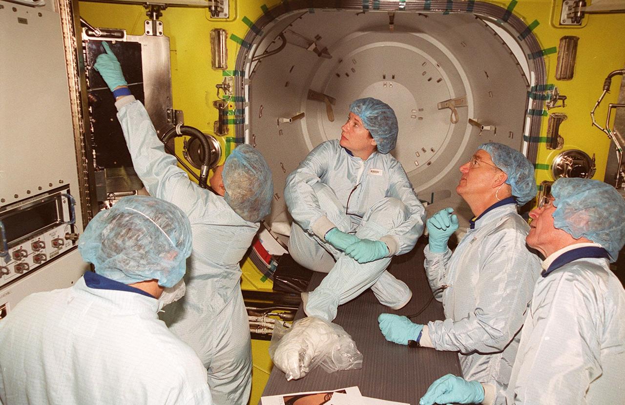 Inside the air lock in the Space Station Processing Facility, a technician points to part of the equipment. Watching her are (left to right) cosmonaut Yury Usachev (back to camera), astronaut Susan Helms (seated), astronauts James Voss and John Young, who flew on mission STS-1. Voss, Helms and Usachev will be flying on mission STS-102, launching March 8, to the International Space Station. The air lock will be carried to the Station during their tenure in space. STS-102 will be Helms’ and Voss’s fifth Shuttle flight, and Usachev’s second. They will be replacing the Expedition One crew (Bill Shepherd, Yuri Gidzenko and Sergei Krikalev), who will return to Earth March 20 on Discovery along with the STS-102 crew