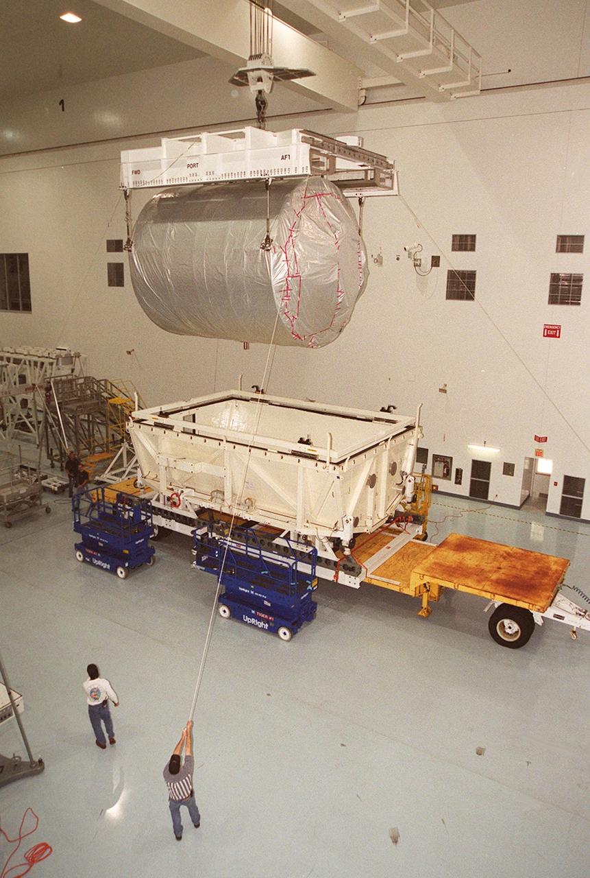 In the Space Station Processing Facility, workers help guide the overhead crane as it lifts the Multi-Purpose Logistics Module Donatello out of the shipping container. In the SSPF, Donatello will undergo processing by the payload test team, including integrated electrical tests with other Station elements in the SSPF, leak tests, electrical and software compatibility tests with the Space Shuttle (using the Cargo Integrated Test equipment) and an Interface Verification Test once the module is installed in the Space Shuttle’s payload bay at the launch pad. The most significant mechanical task to be performed on Donatello in the SSPF is the installation and outfitting of the racks for carrying the various experiments and cargo. Donatello will be launched on mission STS-130, currently planned for September 2004