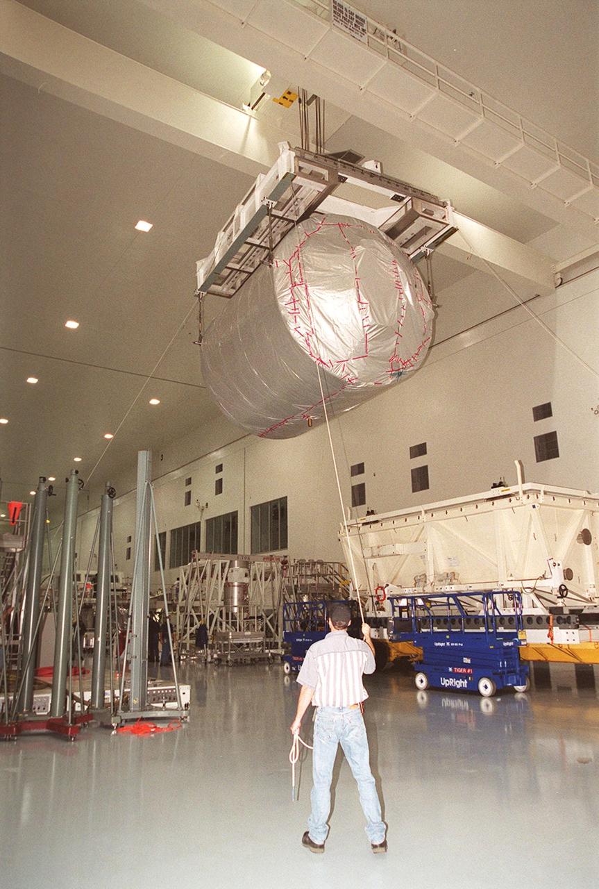 In the Space Station Processing Facility, workers help guide the Multi-Purpose Logistics Module Donatello as it moves the length of the SSPF toward a workstand. In the SSPF, Donatello will undergo processing by the payload test team, including integrated electrical tests with other Station elements in the SSPF, leak tests, electrical and software compatibility tests with the Space Shuttle (using the Cargo Integrated Test equipment) and an Interface Verification Test once the module is installed in the Space Shuttle’s payload bay at the launch pad. The most significant mechanical task to be performed on Donatello in the SSPF is the installation and outfitting of the racks for carrying the various experiments and cargo. Donatello will be launched on mission STS-130, currently planned for September 2004